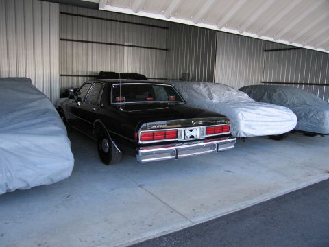 1991 Ford LTD Crown Victoria - A black Chevrolet Caprice sedan is parked in a storage unit alongside other vehicles covered with tarps.