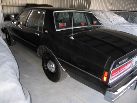1991 Ford LTD Crown Victoria - Black sedan parked indoors, possibly a police car or taxi, with covers on other vehicles nearby.