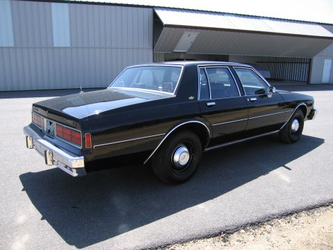 1991 Ford LTD Crown Victoria - This black sedan, identified as a Caprice, is viewed from the rear 3/4 angle in front of a large building.