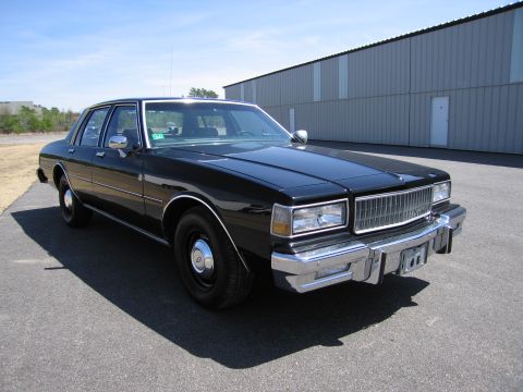 1991 Ford LTD Crown Victoria - This black sedan is parked in front of a large industrial building on a sunny day.
