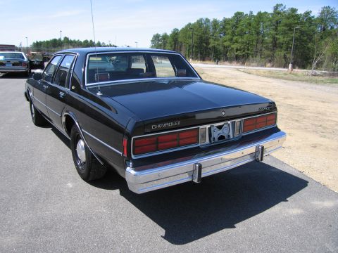1991 Ford LTD Crown Victoria - Rear view of a black Chevrolet Caprice sedan. A second vehicle is partially visible in the background.
