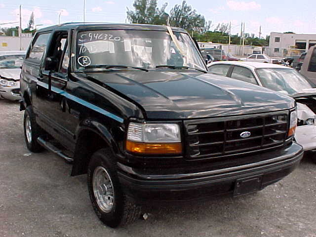 Black 1990s Ford Bronco at a salvage yard with soap-marked windshield and stock numbers