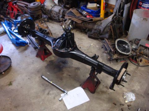 1989 Ford Bronco - Rear axle assembly supported by jack stands, with various automotive parts scattered around the garage floor.