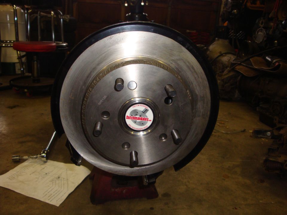 Close-up of a vehicle's brake rotor and hub assembly, with a 'DutchmanAxles.com' sticker in the center