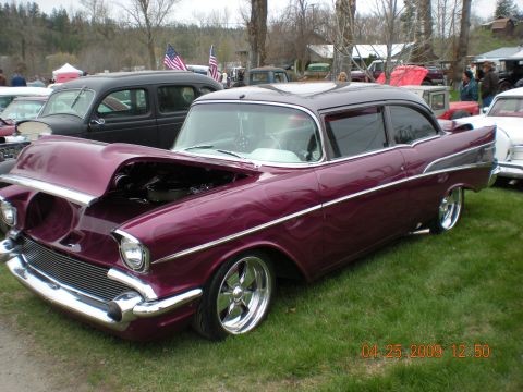 1974 Ford Ranchero - Customized 1957 Chevrolet Bel Air with flames paint and open hood at an outdoor car show.