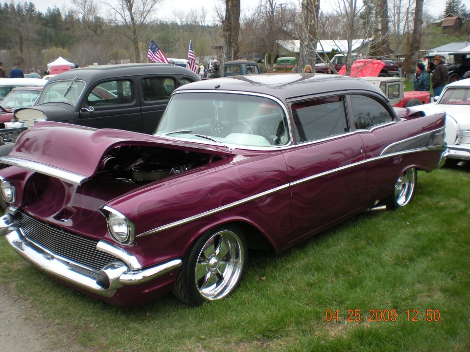 Customized 1957 Chevrolet Bel Air with purple flames paint, hood open, parked on grass