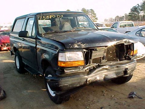 1983 Ford Bronco - This damaged black SUV is parked in an outdoor lot with other vehicles visible in the background.