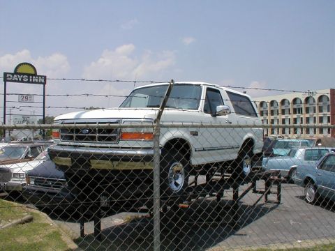 1983 Ford Bronco - White Ford Bronco is elevated on a platform in front of a Days Inn. Other vehicles are parked nearby.