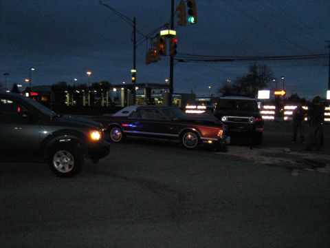 1988 Mercury Grand Marquis - A maroon coupe with a white vinyl roof is parked at an intersection at dusk, with other vehicles nearby.