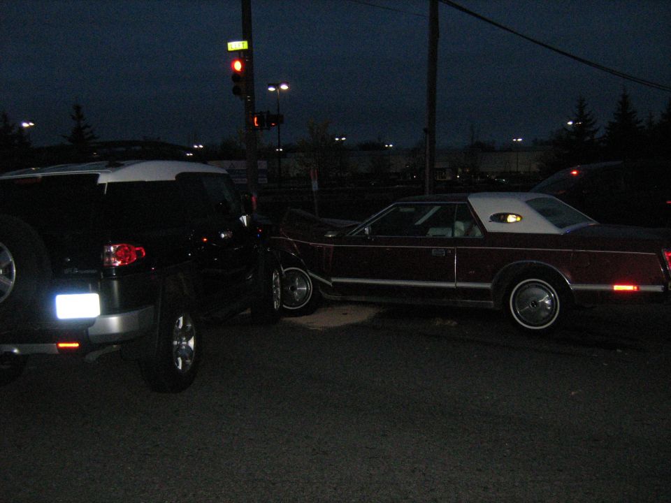 Black Toyota FJ Cruiser and a maroon 1977 Lincoln Continental Mark V at an intersection