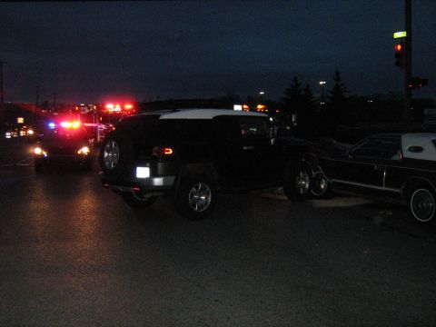 1988 Mercury Grand Marquis - A Hummer H3 and a Lincoln Town Car are parked on a wet road at night, with emergency lights flashing in the distance.