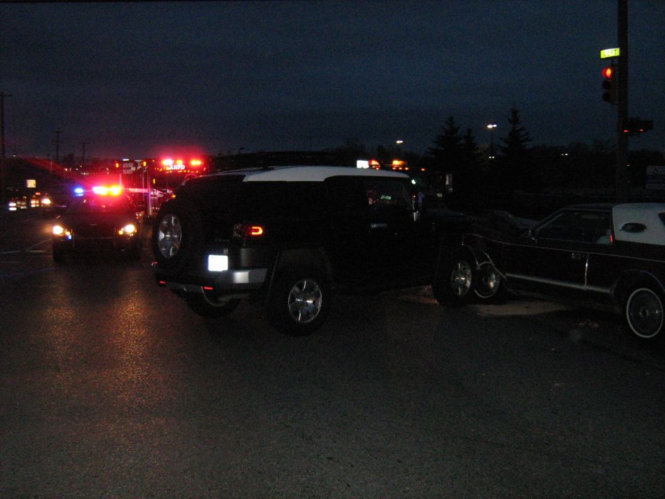 Black Hummer H3 and a dark Lincoln Town Car at night with police lights in the background