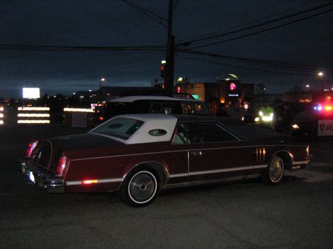 1988 Mercury Grand Marquis - A maroon and white coupe with a vinyl roof is parked at night, with police lights visible in the background.