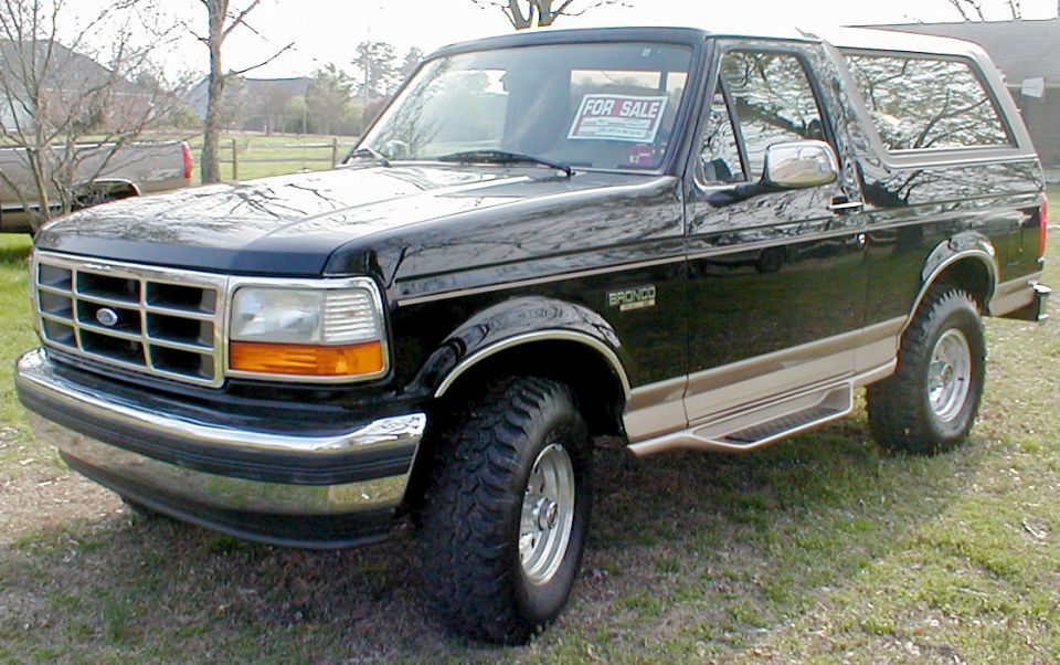 Black two-door Ford Bronco SUV with for-sale sign, parked on grass, front 3/4 view