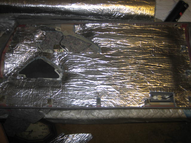 car door panel covered in silver sound deadening material, showing cutouts for speaker and window mechanism