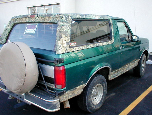 Green Ford Bronco with camouflage soft top and spare tire on rear carrier