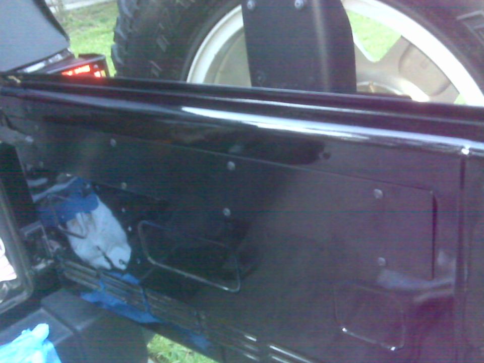 Rear interior panel of a Jeep Wrangler with a spare tire visible above. Some blue and white cloths are tucked inside