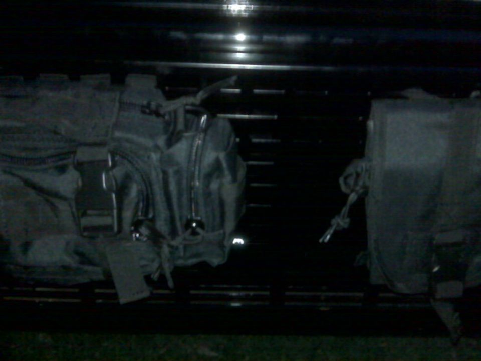 Two black molle pouches attached to a dark, slatted rack
