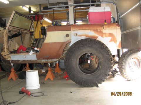 1961 International Scout 800 - A vehicle is being worked on in a garage, supported by jack stands, with its doors open and body in disrepair.