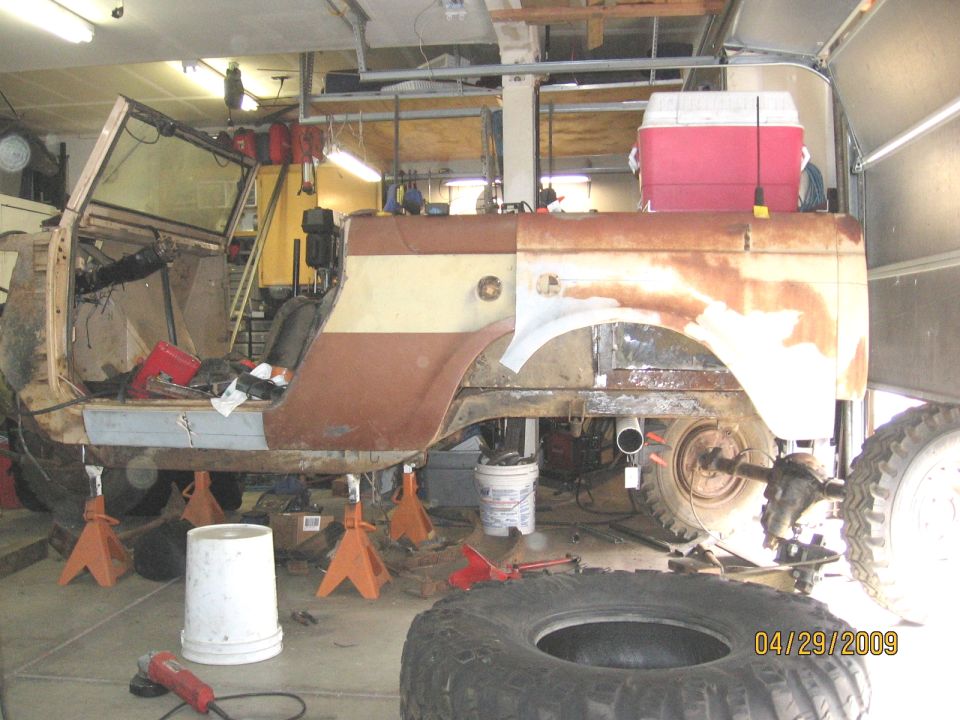 1961 International Scout 800 body on jack stands, undergoing repairs, with rust and primer visible