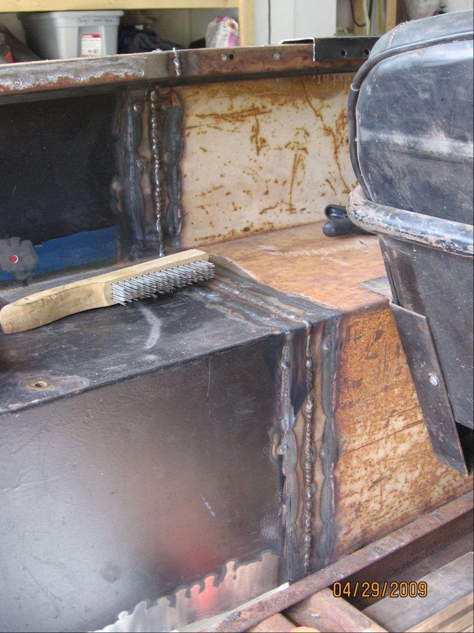 Welding on a vehicle's rusty frame with a wire brush nearby