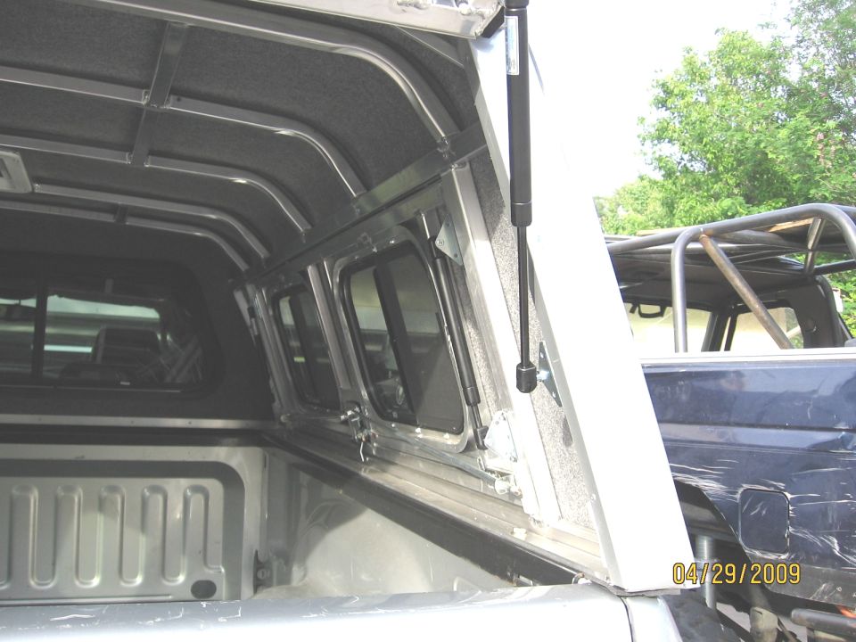 Camper shell interior with windows and gas struts, another truck visible