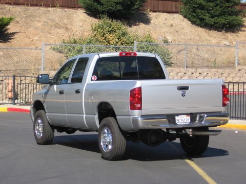 2007 Dodge 2500 - A silver Dodge Ram pickup truck is parked on asphalt with a chain-link fence and hillside in the background.