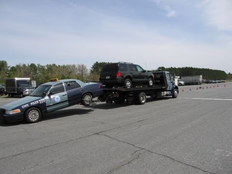 2001 Ford Crown Victoria - A tow truck transports a Massachusetts State Police car, with a dark SUV also on the flatbed.
