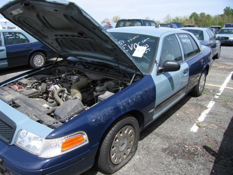 2001 Ford Crown Victoria - A two-tone blue Ford Crown Victoria is parked with its hood open, revealing the engine bay. A flat tire is visible on the front passenger s…