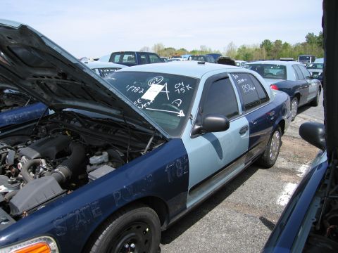 2001 Ford Crown Victoria - A two-tone blue 2001 Ford Crown Victoria, marked "STATE POLICE", sits in a lot with its hood open.