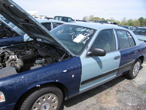 2001 Ford Crown Victoria - A two-tone police car sits in a lot with its hood open. Writing on the windshield indicates 'EVAC' and '2003'.