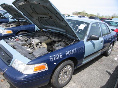 2001 Ford Crown Victoria - A 2001 Ford Crown Victoria police car is shown with its hood open, revealing the engine compartment. Multiple similar vehicles are visible…