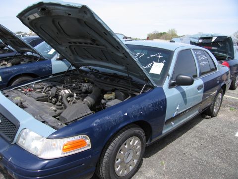 2001 Ford Crown Victoria - A two-tone Ford Crown Victoria sits in a lot with its hood open, revealing the engine compartment.