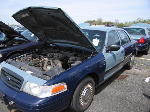 2001 Ford Crown Victoria - A two-tone blue Ford Crown Victoria, likely a former police vehicle, is parked with its hood open, revealing the engine.