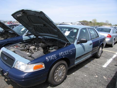 2001 Ford Crown Victoria - A police car, possibly a Ford Crown Victoria, is parked with its hood open, revealing the engine compartment. Text on the door reads "STATE…