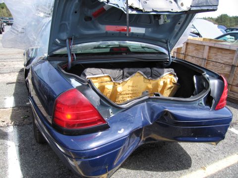 2001 Ford Crown Victoria - Rear view of a blue 2001 Ford Crown Victoria with significant damage to the right rear quarter panel and open trunk.
