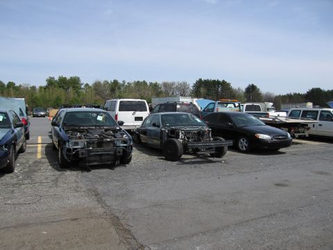 2001 Ford Crown Victoria - Multiple vehicles, some heavily damaged and stripped, are parked outdoors in a lot.