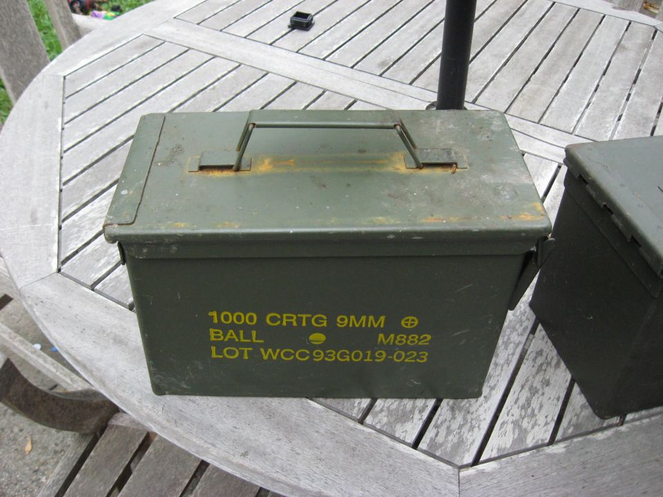 Olive drab military ammo can stenciled 1000 CRTG 9MM BALL M882 on a teak patio table