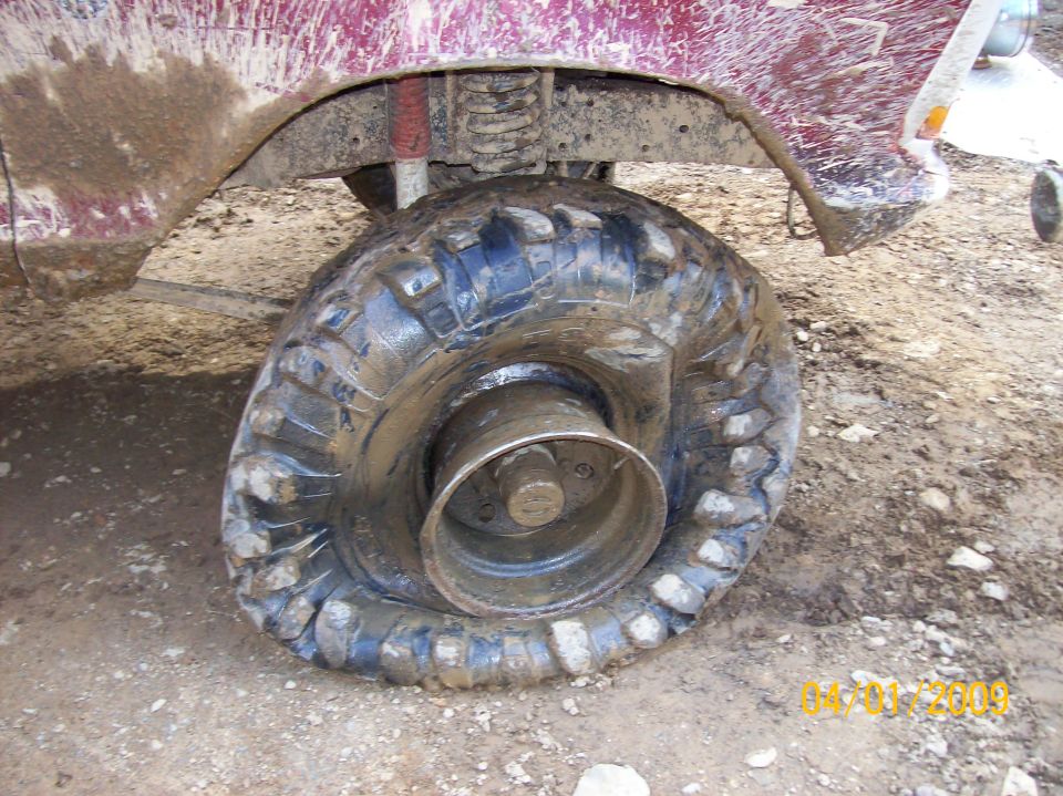 Flat deflated mud tire on steel wheel under a muddy lifted red truck