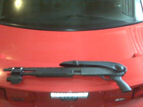 2004 Ford Mustang - A shotgun rests on the hood of a red 2004 Ford Mustang, with 'SUPERMOTORS' visible on the lower right.