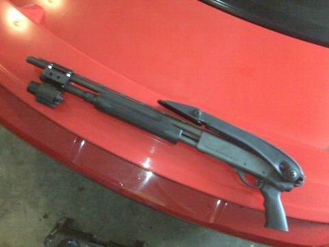 2004 Ford Mustang - A shotgun with a flashlight attachment rests on the hood of a red vehicle.