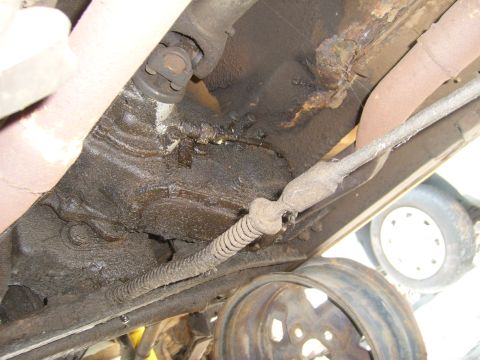 1994 Ford Bronco - The underside of a vehicle shows drivetrain components, rust, and a spare tire in the background.