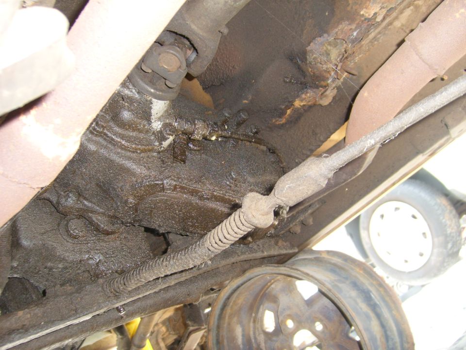 Underside view of vehicle drivetrain with rust and a visible tire
