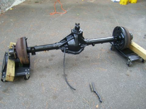 1994 Ford Bronco - Rear axle assembly with drum brakes, resting on dollies outdoors.