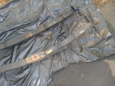 1994 Ford Bronco - Leaf springs, possibly for an off-road vehicle, are shown on a tarp. tarp. One spring is marked 'TOP 100' and the other 'BDS'.