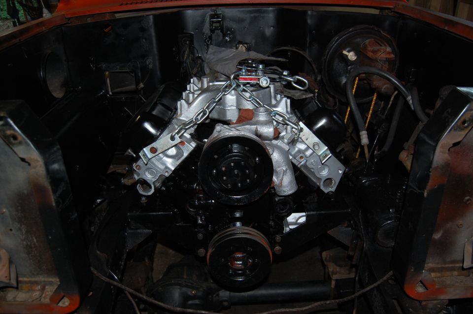 V8 engine installed in engine bay, held by chains. Black pulleys and black engine components visible