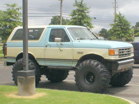 1983 Ford Bronco - This lifted SUV features a two-tone blue and tan paint scheme and aggressive off-road tires. The grille design indicates it is likely from…