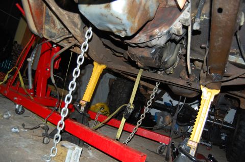 1994 Ford Bronco - Vehicle undercarriage being supported by mechanical equipment, with chains and straps visible.
