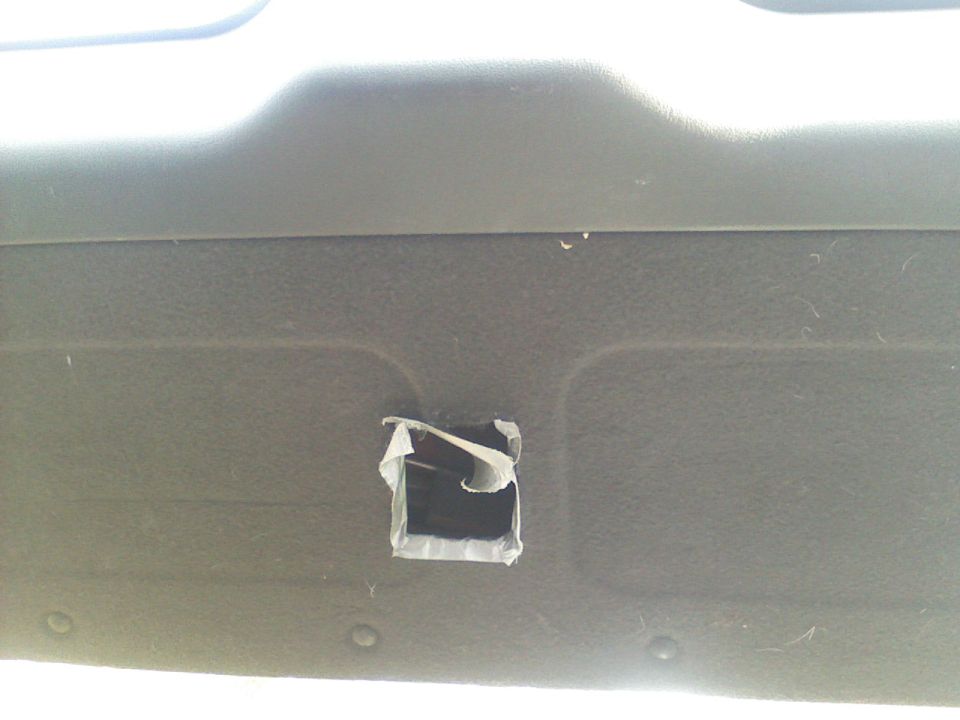 Square hole cut in dark gray interior trim panel with taped edges