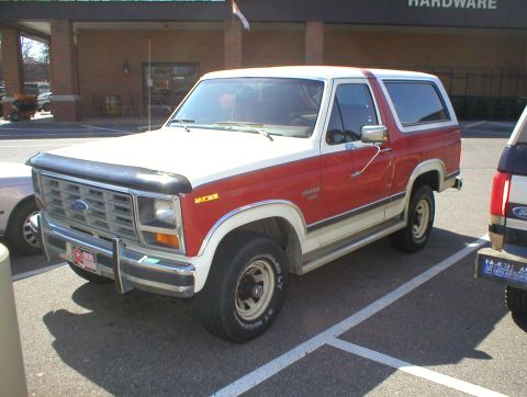 1983 Ford Bronco - This two-tone Ford Bronco is parked next to another vehicle in a parking lot.